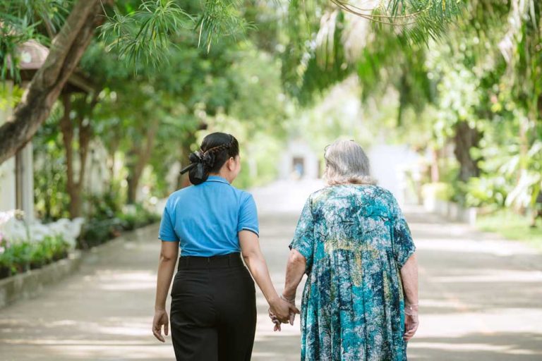 Professional caregiver holding hands and walking with elderly resident at Homerly