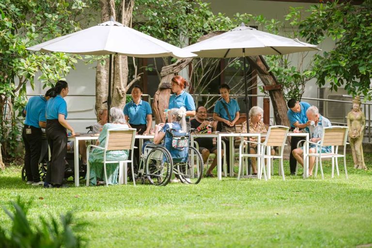 Group of senior residents enjoying healthy outdoor garden lunch with caring staff
