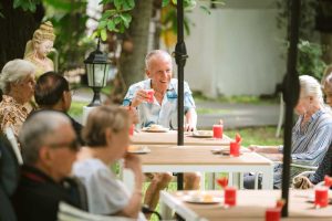 Joyful senior man raising his juice glass during outdoor community lunch in Thailand