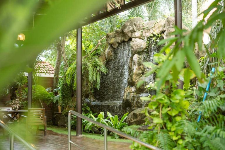 Refreshing tropical waterfall and lush green garden at Homerly senior living resort