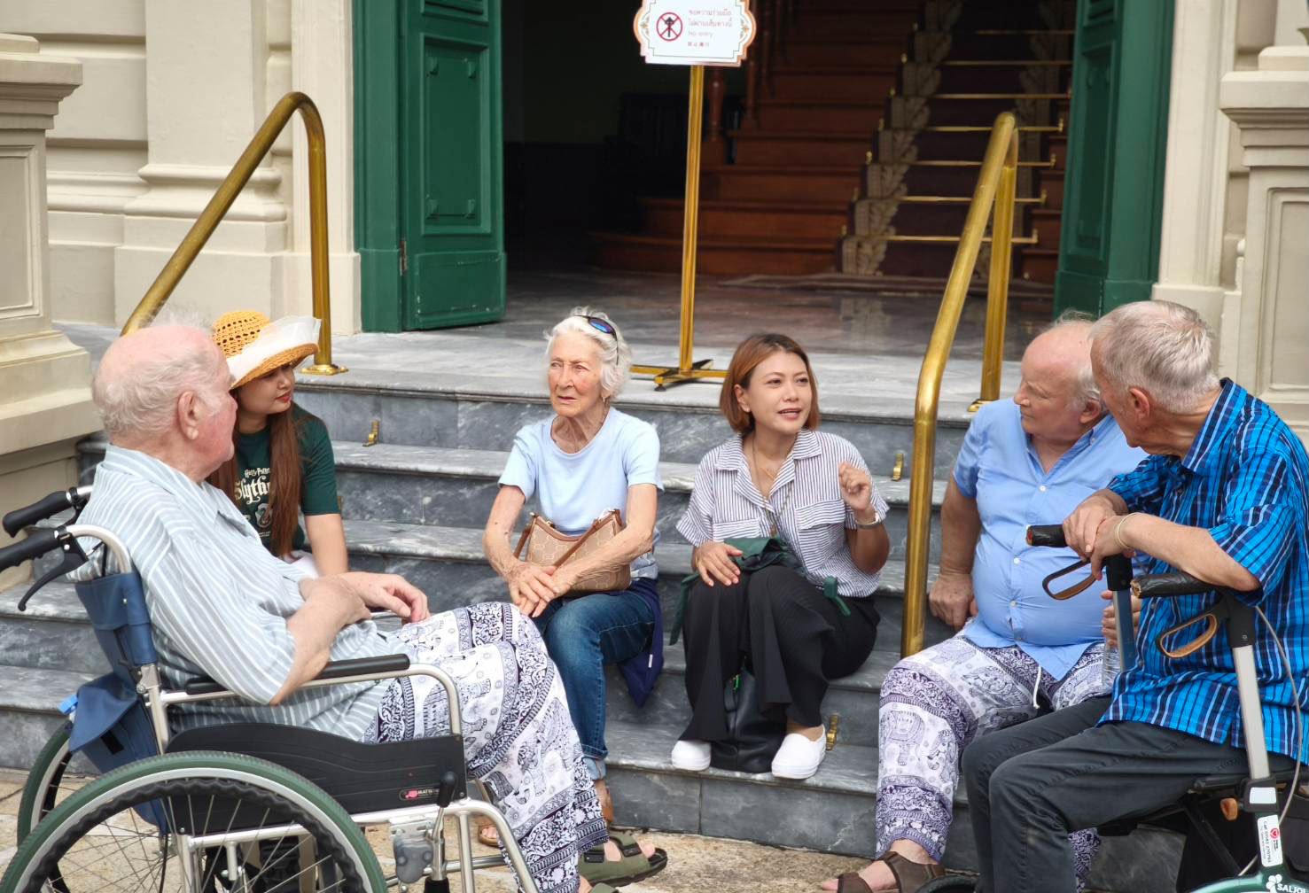 Homerly residents and staff laughing together on the steps of a historic building during the Bangkok trip