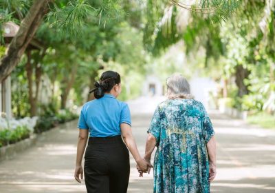 Professional caregiver holding hands and walking with elderly resident at Homerly